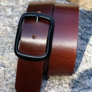 A brown full grian leather belt with a black metal buckle. The belt is folded in half and the buckle is on the top.