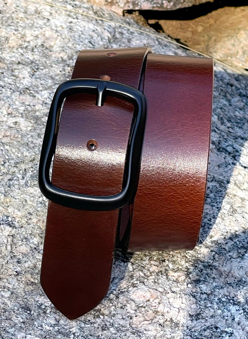 A brown full grian leather belt with a black metal buckle. The belt is folded in half and the buckle is on the top.
