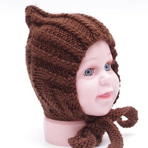 K&ouml;nnte beinhalten: Eine braune gestrickte Baby-M&uuml;tze mit einer spitzen Spitze und einer langen Schleife. Die M&uuml;tze ist aus weichem, dickem Garn gefertigt und hat ein schlichtes, klassisches Design.