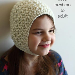 May include: A PDF knitting pattern for a cream-coloured bonnet with a textured design. The bonnet covers the head and ears, with a chin strap. The image text reads "PDF Knitting Pattern" and "sizes: newborn to adult."
