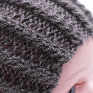 May include: A close-up of a gray knitted beanie hat. The hat is made of a soft, fuzzy yarn and has a simple, classic design.
