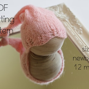 Puede incluir: Un gorro de bebé de punto rosa con una parte superior larga y puntiaguda. El gorro está en una forma de madera y el texto "sizes: newborn to 12 months" es visible en la imagen.