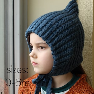 Op de afbeelding: Een kind draagt ​​een blauwe gebreide muts met een strik, de muts heeft een puntige top en is gemaakt met een ribbelsteek. De tekst "sizes: 0-6m to adult" is zichtbaar in de afbeelding.