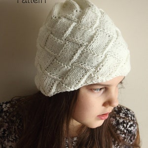 Puede incluir: Un gorro blanco de punto con un patrón tejido. El gorro lo lleva puesto una persona con el pelo largo y castaño. El texto "PDF Knitting Pattern" y "size: teen to adult" es visible en la imagen.