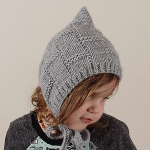 Peut inclure: Un bonnet gris en tricot avec un sommet pointu. Le bonnet a un motif g&eacute;om&eacute;trique et est port&eacute; par un enfant.