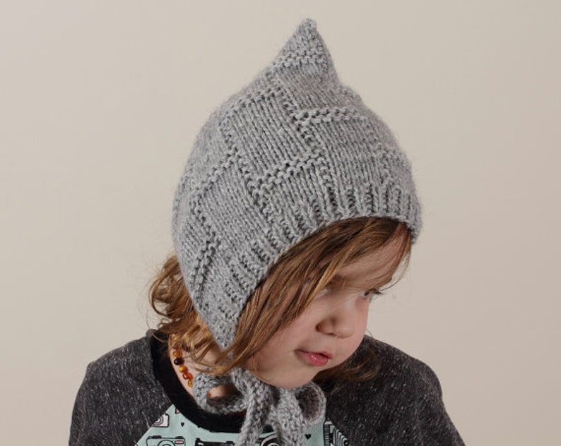 Peut inclure: Un bonnet gris en tricot avec un sommet pointu. Le bonnet a un motif g&eacute;om&eacute;trique et est port&eacute; par un enfant.