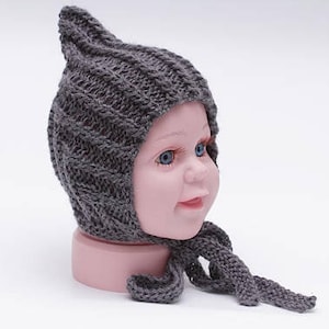 May include: A gray knitted baby bonnet with a pointed top and a long tie. The bonnet is made of a soft, textured yarn and has a simple, classic design.