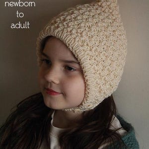 May include: A cream-colored knitted hat with a textured pattern, worn by a person. The hat has a pointed top and covers the ears and forehead. Text at the top of the image reads "PDF Knitting Pattern" and "sizes: newborn to adult."
