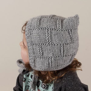 Peut inclure: Un bonnet b&eacute;b&eacute; en tricot gris avec des rabats d'oreilles. Le bonnet a un motif textur&eacute; et est fait de fil doux.