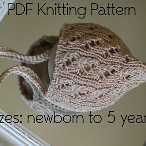 Peut inclure: Un bonnet de bébé beige tricoté avec un motif ajouré détaillé. Le bonnet a des liens et est conçu pour les tailles nouveau-né à 5 ans. Le texte "PDF Knitting Pattern" et "sizes: newborn to 5 years" sont visibles.