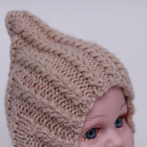 Peut inclure: Un bonnet b&eacute;b&eacute; en tricot beige avec un sommet pointu et un motif en tricot torsad&eacute;.