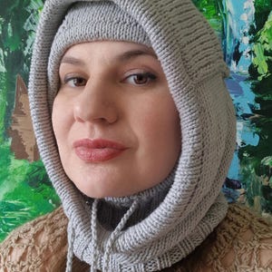 May include: A light grey knitted hood with a drawstring. The hood, made from thick, textured yarn, covers the head and neck. The image includes the text "PDF Knitting Pattern" at the top.
