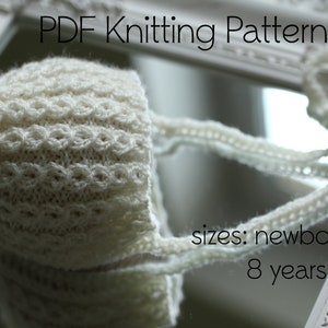 Peut inclure: Bonnet bébé en tricot blanc avec une attache en crochet. Le bonnet est présenté dans un reflet de miroir. Le texte "PDF Knitting Pattern" et "sizes: newborn to 8 years" est visible sur l'image.