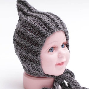 May include: Gray knitted baby hat with a pointed top and a long tie. The hat is made of a soft, warm material and is perfect for keeping a baby's head warm in the winter.