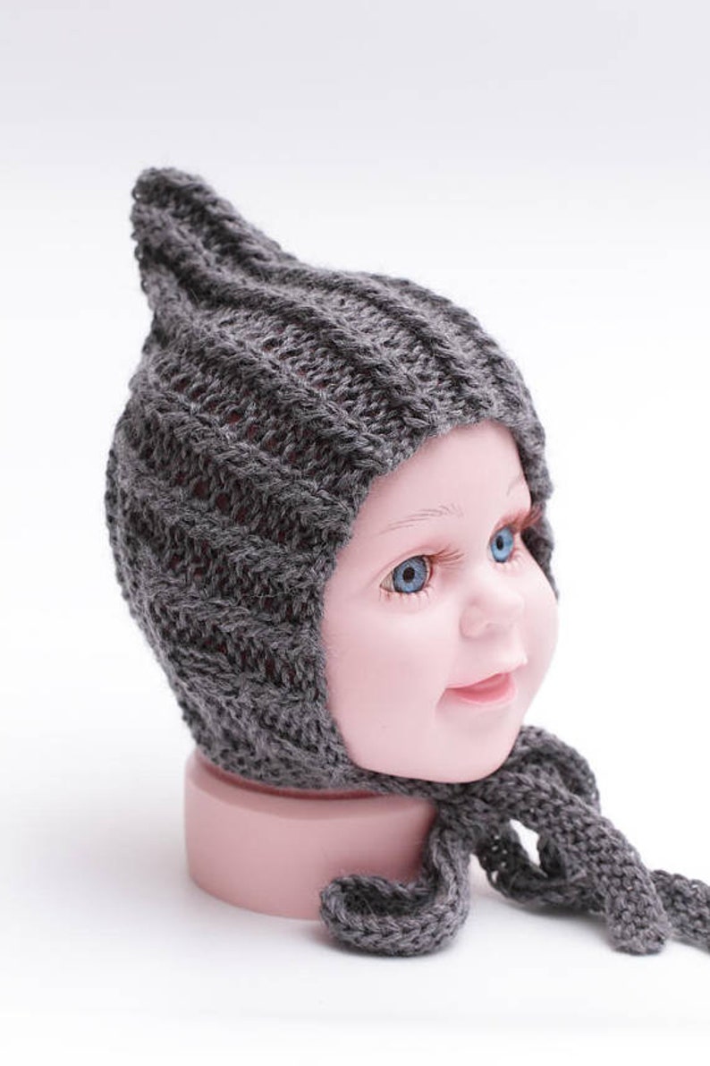May include: Gray knitted baby hat with a pointed top and a long tie. The hat is made of a soft, warm material and is perfect for keeping a baby's head warm in the winter.