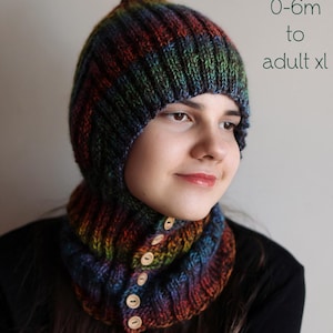 Peut inclure: Ensemble cagoule et cache-cou tricoté multicolore. La cagoule a un sommet pointu et le cache-cou a des boutons en bois. Le texte "PDF Knitting Pattern" et la gamme de tailles "0-6m à adulte xl" sont visibles.