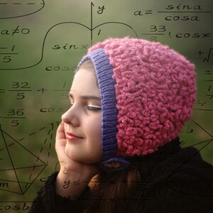 Puede incluir: Una persona joven con un gorro de crochet rosa y morado, mirando pensativamente una pizarra cubierta de ecuaciones matemáticas. Las ecuaciones incluyen funciones trigonométricas, como seno y coseno, y expresiones algebraicas.