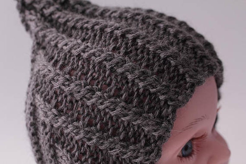 May include: A gray knitted beanie hat with a pointed top. The hat is made of a soft, textured yarn.