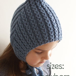 Può includere: Un cappello blu a maglia con la cima a punta e una cravatta. Il cappello è indossato da un bambino e il testo "sizes: newborn to teen" è visibile sotto il cappello.