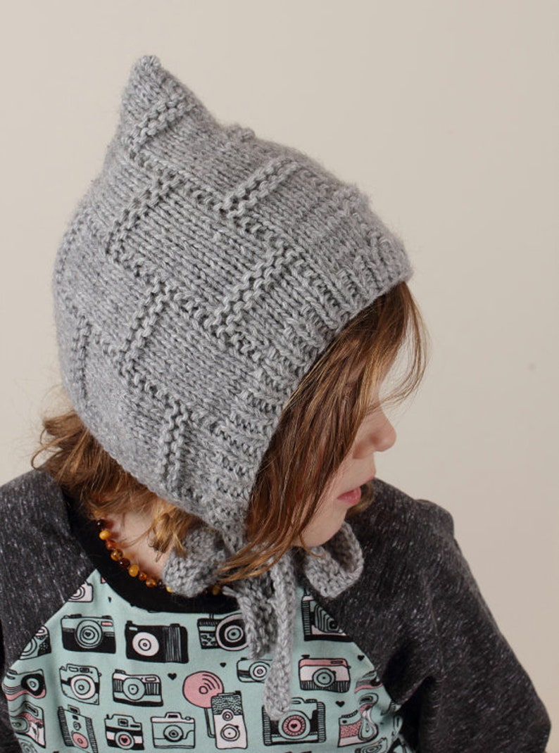 Peut inclure: Un bonnet gris en tricot avec un sommet pointu et une longue cravate. Le bonnet est port&eacute; par un enfant aux cheveux bruns et une chemise &agrave; imprim&eacute; cam&eacute;ra.