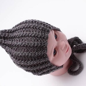 May include: Gray knitted baby hat with a pointed top and a matching scarf. The hat has a ribbed texture and is tied with a long scarf.
