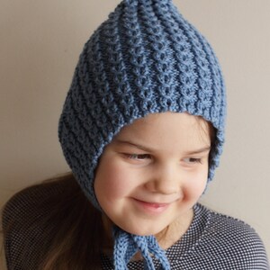 Pu&ograve; includere: Un cappello blu a maglia con la cima a punta e le alette per le orecchie. Il cappello ha un design semplice e testurizzato e si lega sotto il mento.
