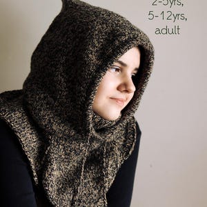 Peut inclure: Gros plan d'une personne portant une cagoule à capuche noire et marron. La cagoule est tricotée et possède une longue capuche flottante. Le texte "sizes: 2-5yrs, 5-12yrs, adult" est visible dans le coin supérieur droit de l'image.