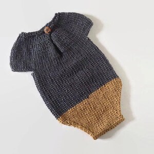 May include: A handmade knitted baby romper in charcoal gray and tan. The romper features short sleeves, a button closure at the shoulder, and a two-tone design. The bottom half is tan, and the top half is charcoal gray.