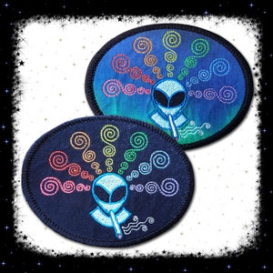 May include: Two embroidered patches featuring an alien smoking a joint with rainbow coloured smoke. The patches are oval shaped and have a black background with white stitching. One patch has a blue background with white stitching.