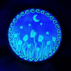 May include: A round, blue canvas with a white crescent moon and stars. The canvas is decorated with a border of white swirls and a field of white mushrooms.