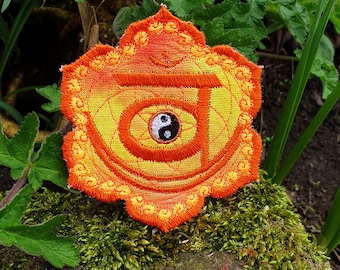 May include: Orange and yellow embroidered chakra patch with a yin yang symbol in the center. The patch is shaped like a flower with multiple layers of petals.