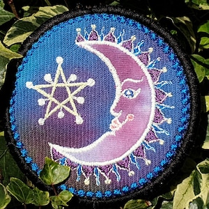 May include: A round, embroidered patch with a crescent moon and a five-pointed star. The moon is pink and purple with a face, and the star is yellow. The background is a gradient of blue and purple.