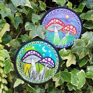 May include: Two embroidered patches featuring mushrooms. The first patch has a blue background with white, red, and green mushrooms. The second patch has a green background with white and purple mushrooms.