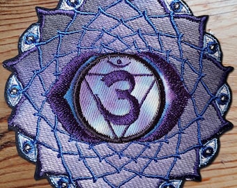 May include: Purple and blue embroidered patch with a stylized eye symbol in the center. The symbol is surrounded by a circle of smaller eyes. The patch is designed to represent the sixth chakra, the third eye chakra.