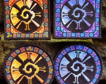 May include: Four embroidered patches featuring a stylized sun symbol with a spiral in the center. Two patches are square with orange, yellow, and blue borders. Two patches are round with orange, yellow, and blue borders.