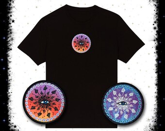 May include: Black t-shirt with a circular design featuring an eye, mushrooms, and a colorful gradient. Two matching patches are displayed below the shirt, one with a purple and orange gradient and the other with a blue and purple gradient.