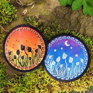 May include: Two round embroidered patches with a mushroom theme. One patch features a sunset with orange, red, and yellow colors and black mushrooms. The other patch features a night sky with blue, purple, and white colors and white mushrooms.