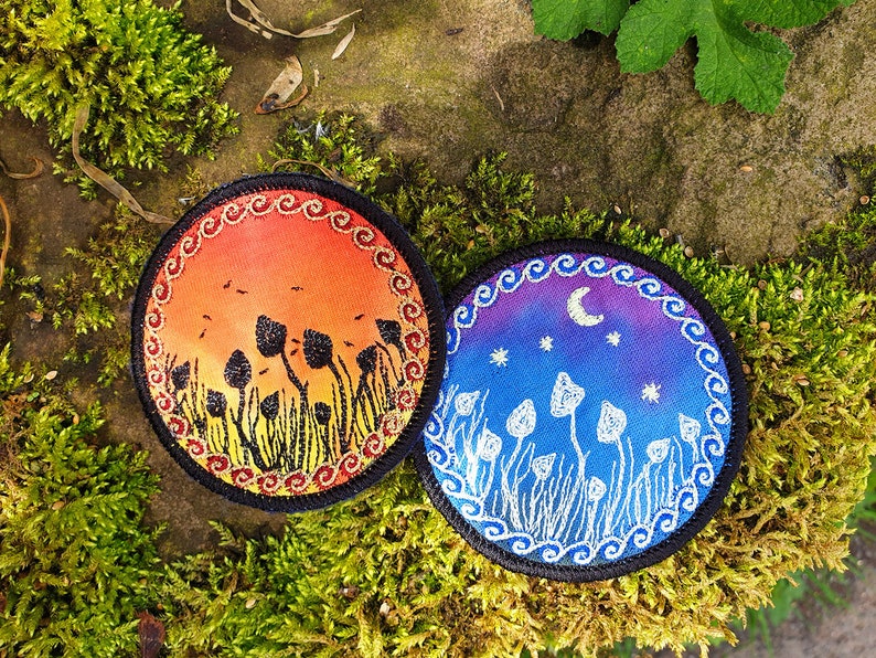 May include: Two round embroidered patches with a mushroom theme. One patch features a sunset with orange, red, and yellow colors and black mushrooms. The other patch features a night sky with blue, purple, and white colors and white mushrooms.