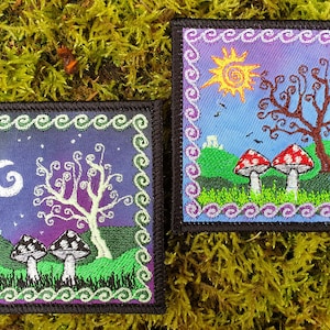 May include: Two embroidered patches depicting a whimsical forest scene. Each patch features a stylised tree with swirling branches, a hill, and two mushrooms. One patch has a blue sky with a yellow sun, while the other has a purple sky with a white moon. Both patches have a green and purple border.