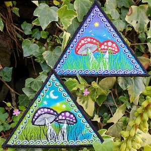 May include: Two embroidered triangular patches with a psychedelic mushroom theme. The top patch features red mushrooms with white spots on a blue background with a yellow sun and white birds. The bottom patch features purple mushrooms with white spots on a green background with a white crescent moon and white stars.