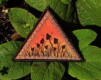 May include: A triangular patch with a black outline and a gold glitter border. The patch features a sunset scene with a field of black silhouette mushrooms.