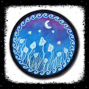 May include: A round embroidered patch with a blue and purple gradient background. The patch features a crescent moon, stars, and white mushrooms in a field of grass. The border of the patch is a black circle with a white, swirling design.