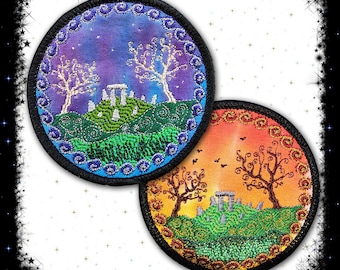 May include: Two round embroidered patches with a nature scene. The first patch has a purple and blue background with a white tree and a stone circle. The second patch has an orange and yellow background with a brown tree and a stone circle.