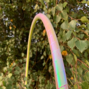 Op de afbeelding: Een close-up van een regenboogkleurige hoepel met een lichtgroen en roze kleurenschema. De hoepel is gemaakt van plastic en heeft een glad oppervlak.