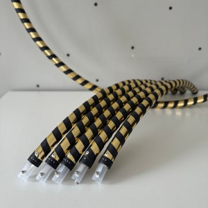 May include: Five black and gold striped hoops with silver ends. The hoops are arranged in a curved shape.