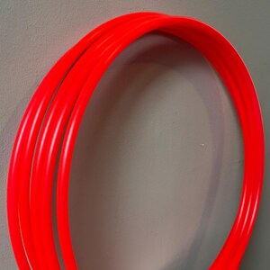 Puede incluir: Primer plano de un tubo de plástico rojo brillante y curvado. El tubo tiene un acabado liso y brillante, que refleja la luz. La imagen se centra en el color vibrante y la forma redondeada del tubo. Probablemente destinado a la artesanía o la decoración.