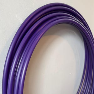 May include: A close-up shot of several loops of a vibrant purple, flexible tubing. The tubing is smooth and appears to be made of a durable material. The loops are arranged in a semi-circular shape, creating a visually appealing pattern.