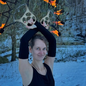 May include: A pair of black metal fire fans with wooden handles and multiple wicks ignited with bright orange flames. The fans feature a star-like geometric frame design with scorched wood accents near the grip area, held aloft in a crossed position.