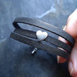 May include: A black leather wrap bracelet with a silver heart charm.