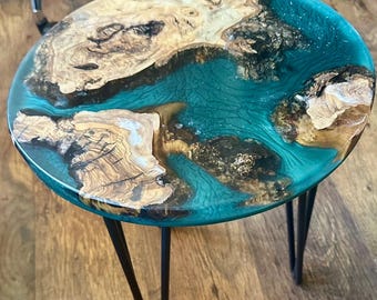 May include: A round wooden table with a teal blue epoxy resin top. The table has three black hairpin legs.